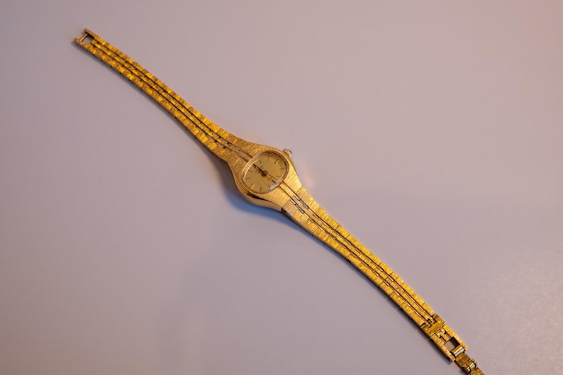 May include: A gold-toned wristwatch with a round face and a gold metal band.