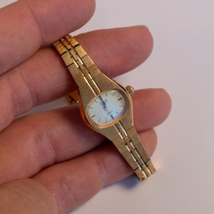 May include: A gold-toned wristwatch with a white face and a gold metal band.