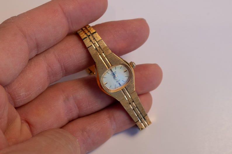 May include: A gold-toned wristwatch with a white face and a gold metal band.