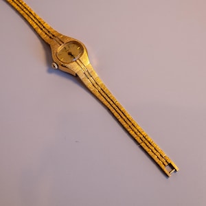 May include: A gold-toned wristwatch with a round face and a gold metal band.
