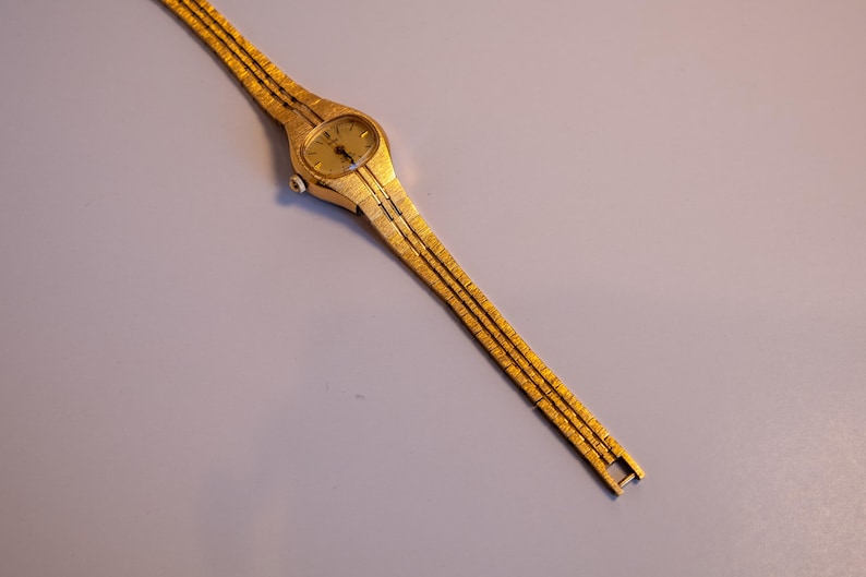 May include: A gold-toned wristwatch with a round face and a gold metal band.