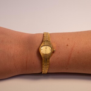 May include: A gold-toned wristwatch with a round face and a gold metal band.