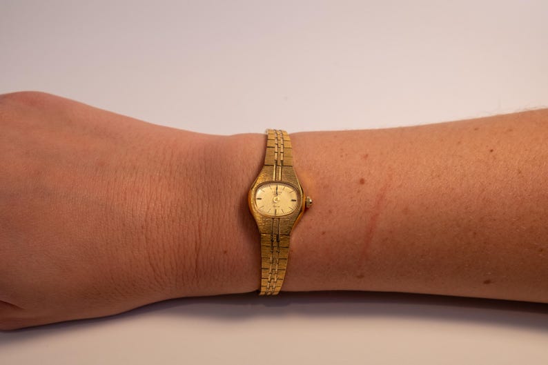 May include: A gold-toned wristwatch with a round face and a gold metal band.