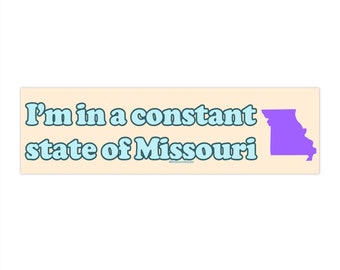 May include: A light beige bumper sticker with the text "I'm in a constant state of Missouri" in light blue letters. The state of Missouri is outlined in purple.
