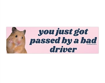 May include: A pink and white bumper sticker with a hamster wearing a peace sign and the text "you just got passed by a bad driver" in navy blue.