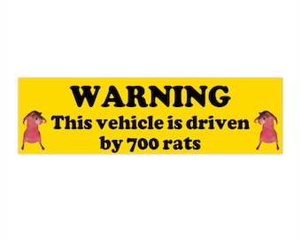 May include: A yellow rectangular sticker with black text that reads "WARNING This vehicle is driven by 700 rats." The sticker has a cartoon image of a pink rat on each side.