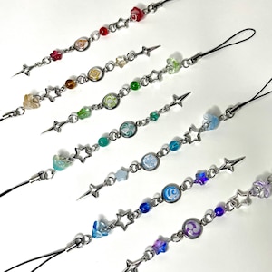 May include: Seven colorful phone charms with star-shaped beads and different colored charms. Each charm has a small, white, decorative design in the center.