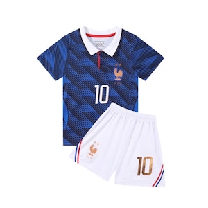 Puede incluir: Un polo azul de manga corta con un patrón diagonal azul oscuro, cuello blanco y el número 10 en blanco. Presenta un emblema de gallo dorado y dos estrellas. Se combina con pantalones cortos blancos con el número 10, un gallo y rayas laterales.
