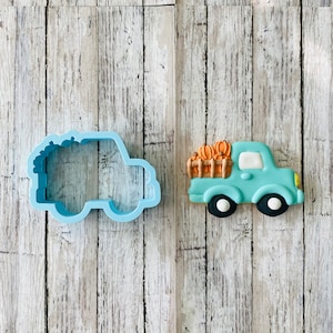 Könnte beinhalten: Ein blauer Ausstecher und ein blau-orangefarbener verzierter Keks in Form eines Pick-up-Trucks, der Kürbisse transportiert.
