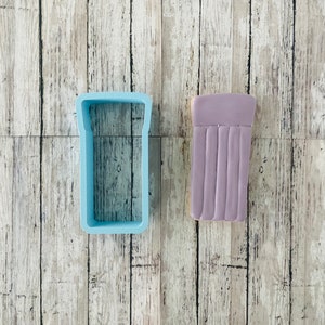 May include: A light blue plastic cookie cutter shaped like a pool float and a purple iced cookie shaped like a pool float.
