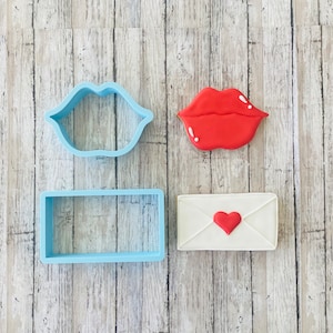 May include: Three cookie cutters: a red lip, a blue rectangle, and a blue lip shape.