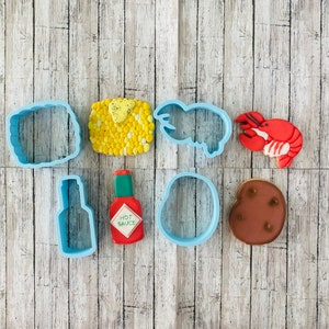 May include: A set of eight blue cookie cutters in various shapes, including a lobster, a bottle, a hot sauce bottle, a corn cob, a crab, a potato, and two rectangles.