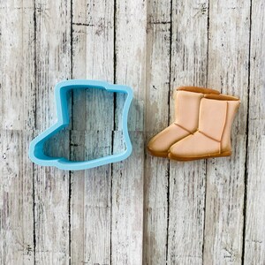 May include: A blue plastic cookie cutter shaped like a boot, and a tan sugar cookie shaped like a boot.