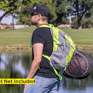 K&ouml;nnte beinhalten: Eine Person tr&auml;gt ein schwarzes T-Shirt und eine schwarze Baseballkappe mit einem gr&uuml;n-grauen Rucksack. Der Rucksack hat ein schwarzes Netz f&uuml;r einen Helm daran befestigt.  "Helmet Net Included" steht in gelber Schrift am unteren Rand des Bildes.