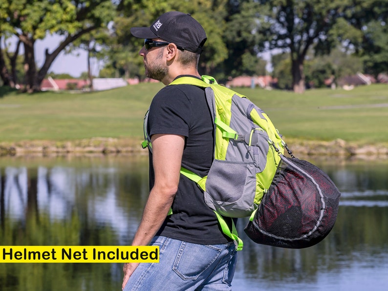 K&ouml;nnte beinhalten: Eine Person tr&auml;gt ein schwarzes T-Shirt und eine schwarze Baseballkappe mit einem gr&uuml;n-grauen Rucksack. Der Rucksack hat ein schwarzes Netz f&uuml;r einen Helm daran befestigt.  "Helmet Net Included" steht in gelber Schrift am unteren Rand des Bildes.