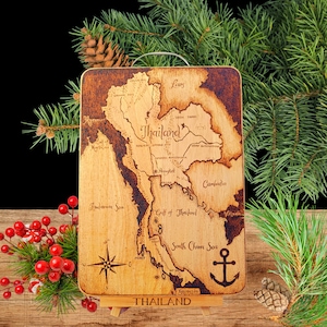May include: Wooden cutting board with a detailed map of Thailand, including the names of cities and bodies of water. The board features a compass rose and an anchor design. The word "THAILAND" is printed at the bottom.