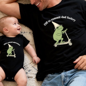 May include: Black t-shirt and onesie set with matching frog graphic riding a scooter and text "Off to commit dad foolery" and "Off to commit mini foolery". The frog wears a wizard hat. The set is for a father and child.