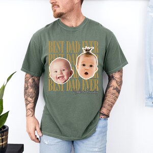 Może przedstawiać: Zielona koszulka w kolorze oliwkowym ze złotym napisem "BEST DAD EVER". Koszulka przedstawia dwie twarze dziecka oraz imiona "Noah & Emily". Koszulka ma swobodny styl.