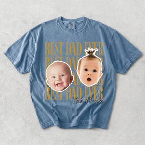 Może przedstawiać: Niebieska koszulka z napisem "BEST DAD EVER" w złotych literach. Koszulka przedstawia dwie twarze dziecka i imiona "Noah & Emily" w skrypcie. Koszulka jest wykonana z miękkiego, wygodnego materiału.