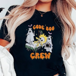 May include: A black t-shirt with a graphic of a skeleton on a hospital bed with ghosts and the text "Code Boo Crew".