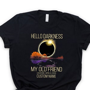 May include: Black t-shirt with a graphic of a solar eclipse and the text "Hello Darkness My Old Friend" with the date "April 8, 2024" and the text "Location/Custom Name".