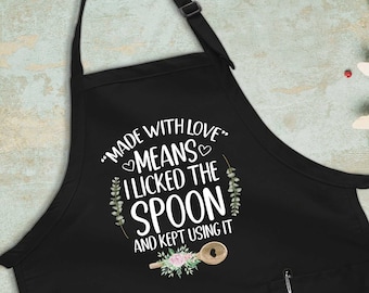 May include: Black apron with a white graphic that says "Made with love means I licked the spoon and kept using it". The graphic also includes a heart, a spoon, and floral accents.