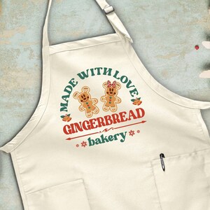 May include: White apron with a red, green, and yellow design. The design features two gingerbread people and the text "Made with Love Gingerbread bakery".