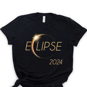 May include: Black t-shirt with a gold graphic of a solar eclipse and the text "ECLIPSE 2024".