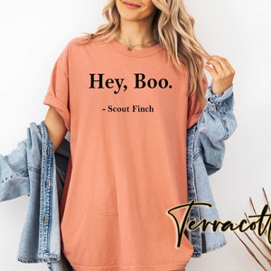 May include: A peach-colored t-shirt with the text "Hey, Boo." and "Scout Finch" printed in black.