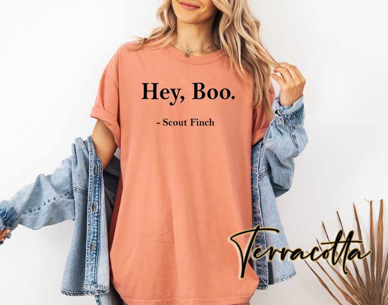May include: A peach-colored t-shirt with the text "Hey, Boo." and "Scout Finch" printed in black.