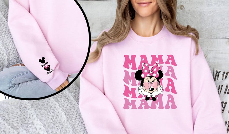 Puede incluir: Sudadera rosa con un gr&aacute;fico de Minnie Mouse con gafas de sol y la palabra "MAMA" repetida en una fuente retro. Las mangas tienen un peque&ntilde;o gr&aacute;fico bordado de Minnie Mouse con los nombres "Oliver" y "Sarah" en los pu&ntilde;os.