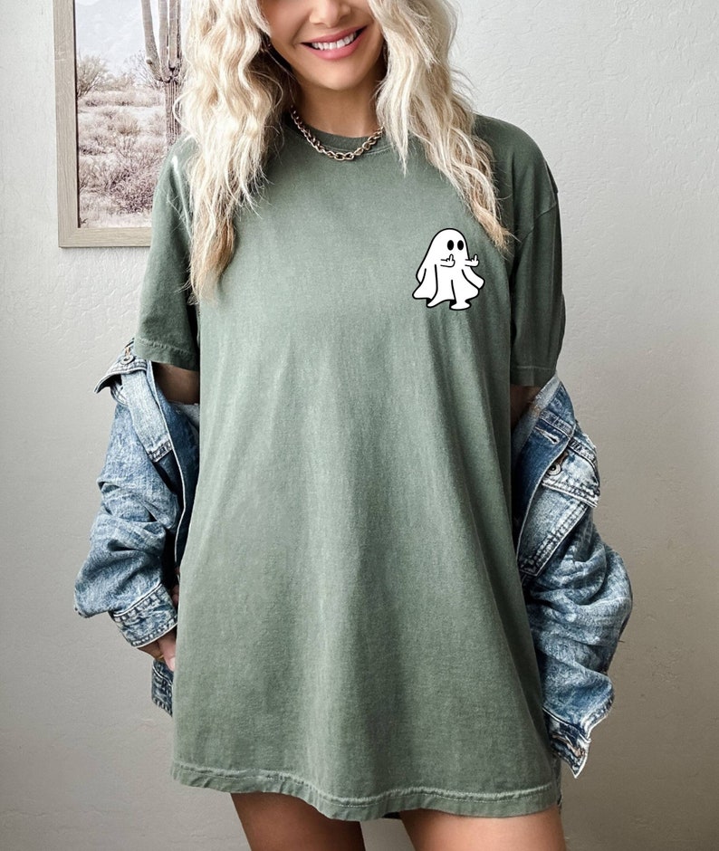 May include: A green t-shirt with a white ghost graphic giving a thumbs up. The ghost has two black eyes.