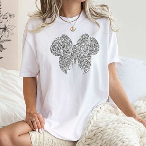 May include: A white t-shirt with a black glitter bow design.