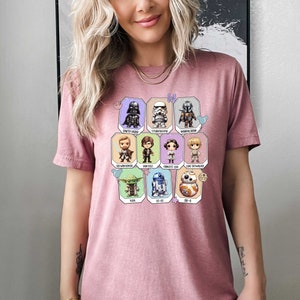 May include: Pink t-shirt with a graphic of Star Wars characters in a grid pattern. The characters include Darth Vader, Stormtrooper, Mandalorian, Obi-Wan Kenobi, Han Solo, Princess Leia, Luke Skywalker, Yoda, R2-D2, and BB-8.