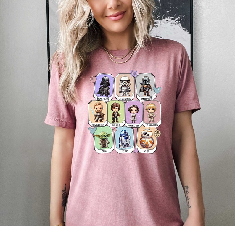 May include: Pink t-shirt with a graphic of Star Wars characters in a grid pattern. The characters include Darth Vader, Stormtrooper, Mandalorian, Obi-Wan Kenobi, Han Solo, Princess Leia, Luke Skywalker, Yoda, R2-D2, and BB-8.