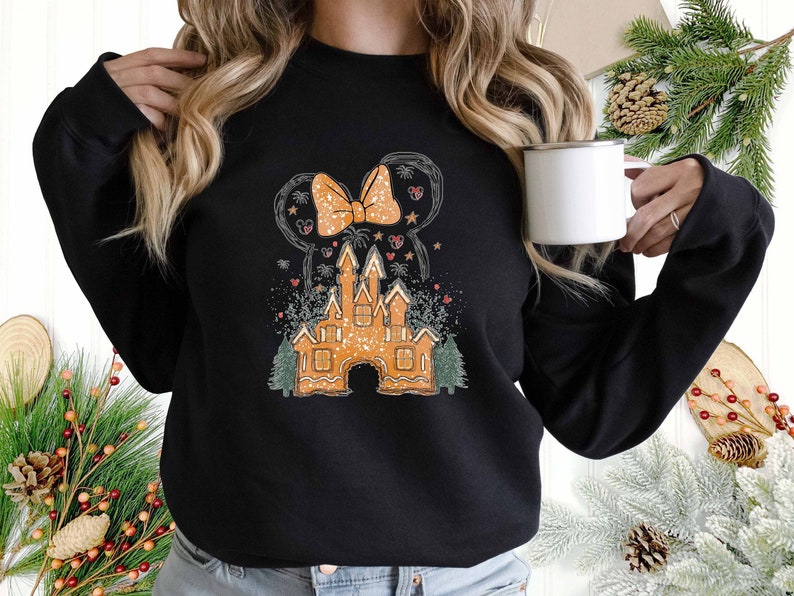 Puede incluir: Sudadera negra con un castillo de jengibre y un lazo de Minnie Mouse. El castillo est&aacute; decorado con chispas blancas y el lazo es rojo y blanco.