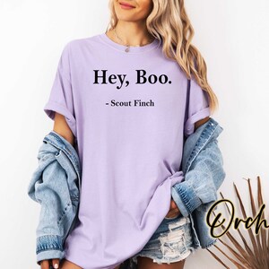 May include: A lavender t-shirt with the text "Hey, Boo." and "Scout Finch" printed on it.