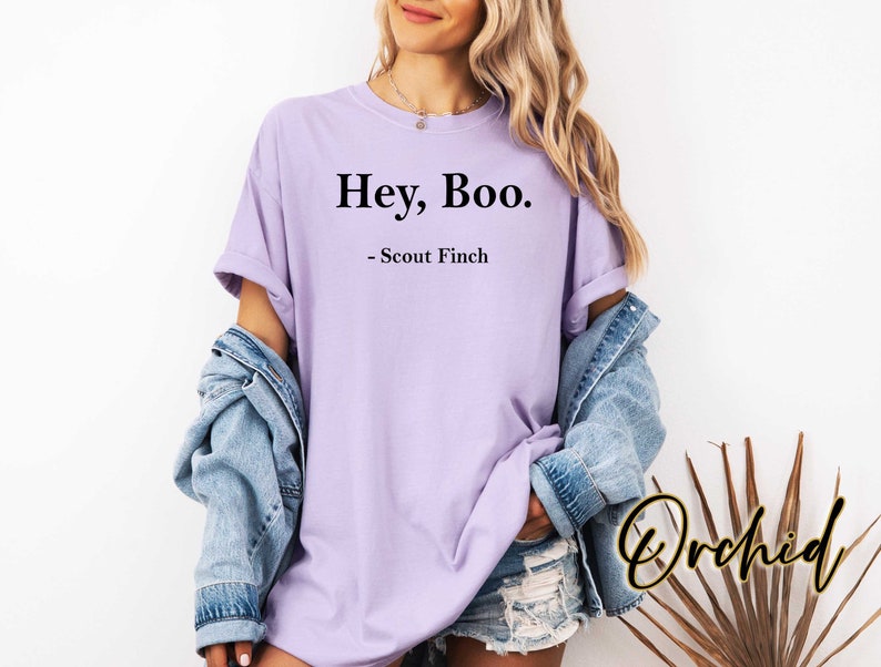 May include: A lavender t-shirt with the text "Hey, Boo." and "Scout Finch" printed on it.