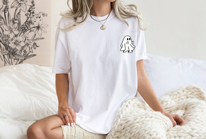 May include: White t-shirt with a small black ghost graphic on the left chest. The ghost is giving a thumbs up.