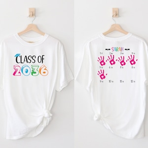May include: White t-shirt with the text "CLASS OF 2036" on the front and the text "SARAH" and a series of pink handprints with numbers representing months on the back.