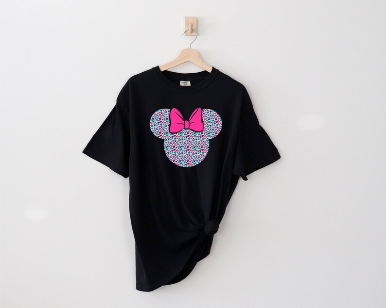 以下が含まれることがあります： カラフルなミニーマウスの頭のグラフィックがプリントされた黒いTシャツ。グラフィックは小さなカラフルなドットで構成されており、ピンクのリボンが付いています。
