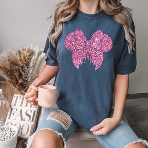 May include: A navy blue t-shirt with a pink glitter bow and castle design. The shirt is oversized and has short sleeves.