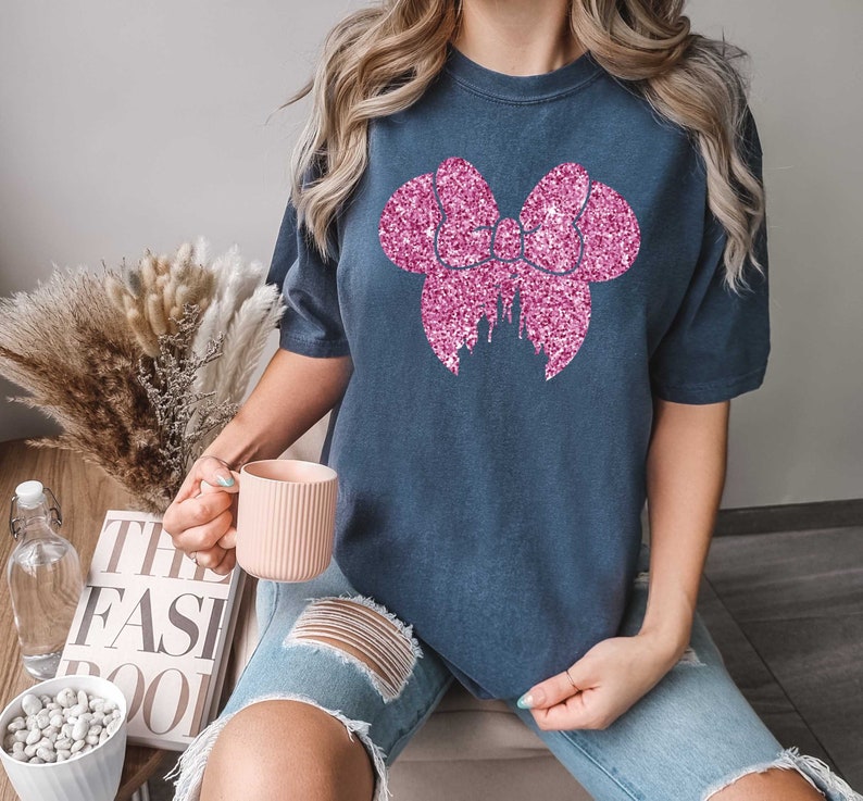 May include: A navy blue t-shirt with a pink glitter bow and castle design. The shirt is oversized and has short sleeves.