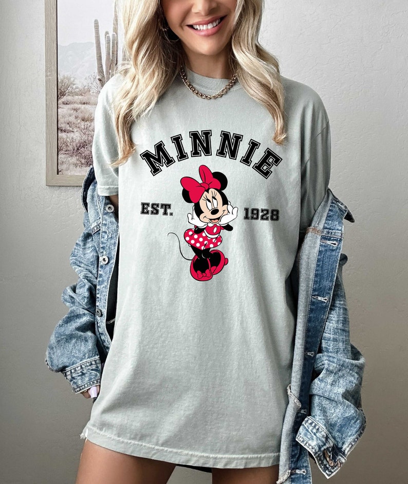 May include: A light green t-shirt with a black and white graphic of Minnie Mouse. The graphic includes the text "MINNIE EST. 1928".