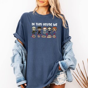May include: A blue t-shirt with the text "In this house we" and a row of cartoon horror movie characters. The characters include Jason Voorhees, Freddy Krueger, Michael Myers, and others.
