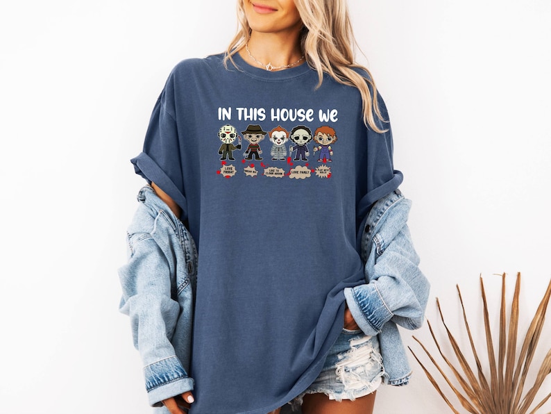 May include: A blue t-shirt with the text "In this house we" and a row of cartoon horror movie characters. The characters include Jason Voorhees, Freddy Krueger, Michael Myers, and others.