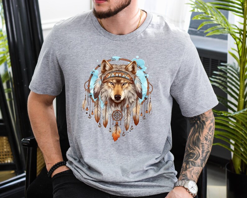 Pode incluir: Camiseta cinza com um gr&aacute;fico de um lobo usando uma coroa de apanhadores de sonhos. O lobo &eacute; marrom e branco com olhos azuis.