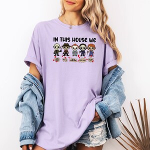 May include: A purple t-shirt with the text "In this house we" and a row of cartoon horror characters. The characters include Jason Voorhees, Michael Myers, Freddy Krueger, and Chucky.