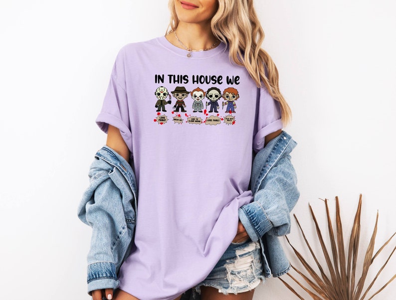 May include: A purple t-shirt with the text "In this house we" and a row of cartoon horror characters. The characters include Jason Voorhees, Michael Myers, Freddy Krueger, and Chucky.