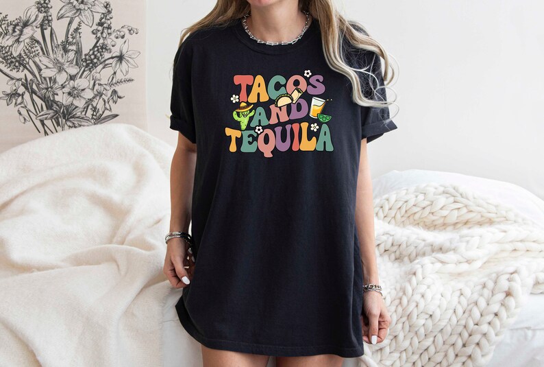Puede incluir: Camiseta negra con un gr&aacute;fico colorido que dice "Tacos and Tequila" con un cactus, tacos y una copa de margarita.